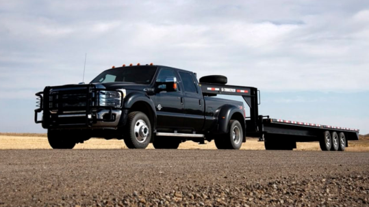 Black dually pickup truck towing gooseneck flatbed trailer