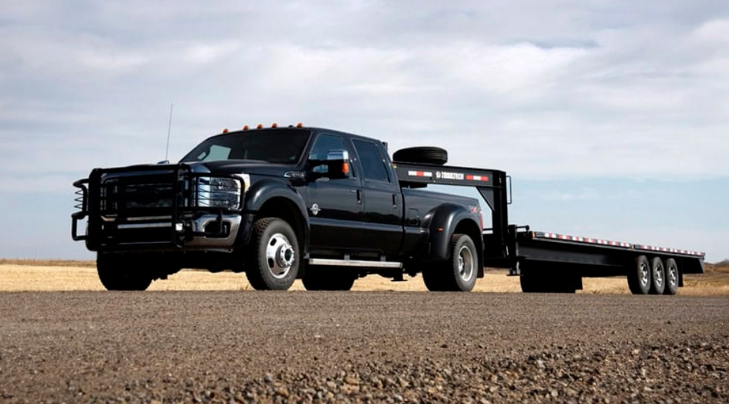 Black dually pickup truck towing gooseneck flatbed trailer
